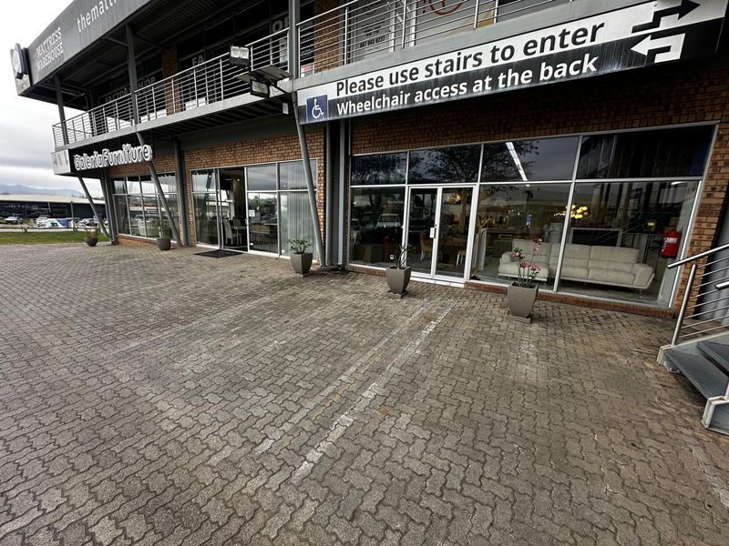 Front exterior view of a retail commercial property featuring a brick facade, large glass storefront windows, and a paved parking area.