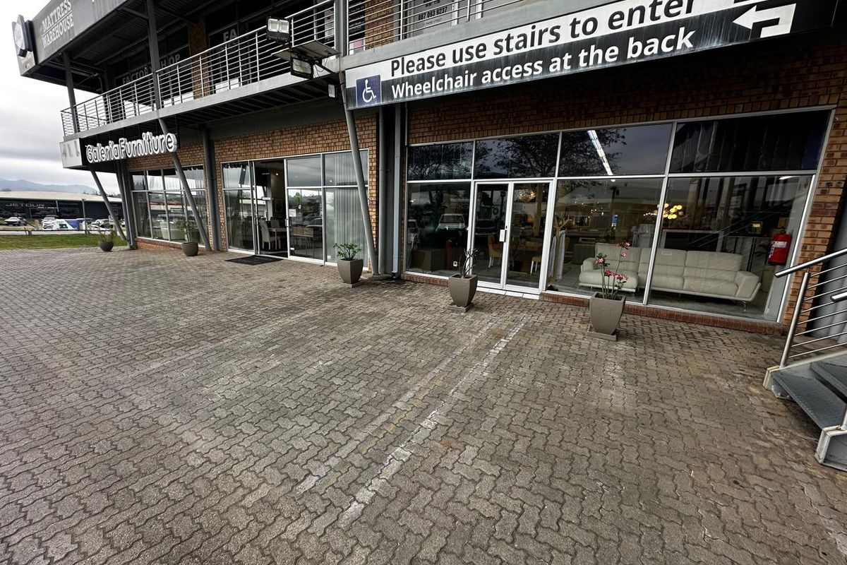 Front exterior view of a retail commercial property featuring a brick facade, large glass storefront windows, and a paved parking area.