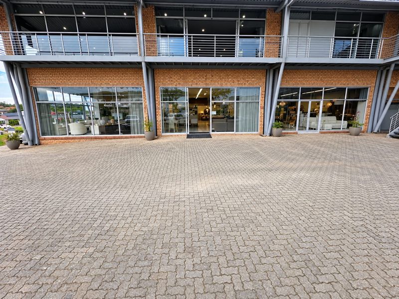 Front view of a modern commercial retail building featuring a brick facade, large glass storefront windows, and a paved entrance area.