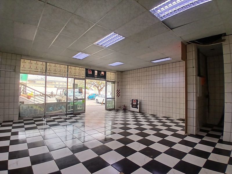 Empty retail space featuring a black and white checkered tiled floor, tiled walls, and a suspended ceiling with integrated fluorescent lighting.