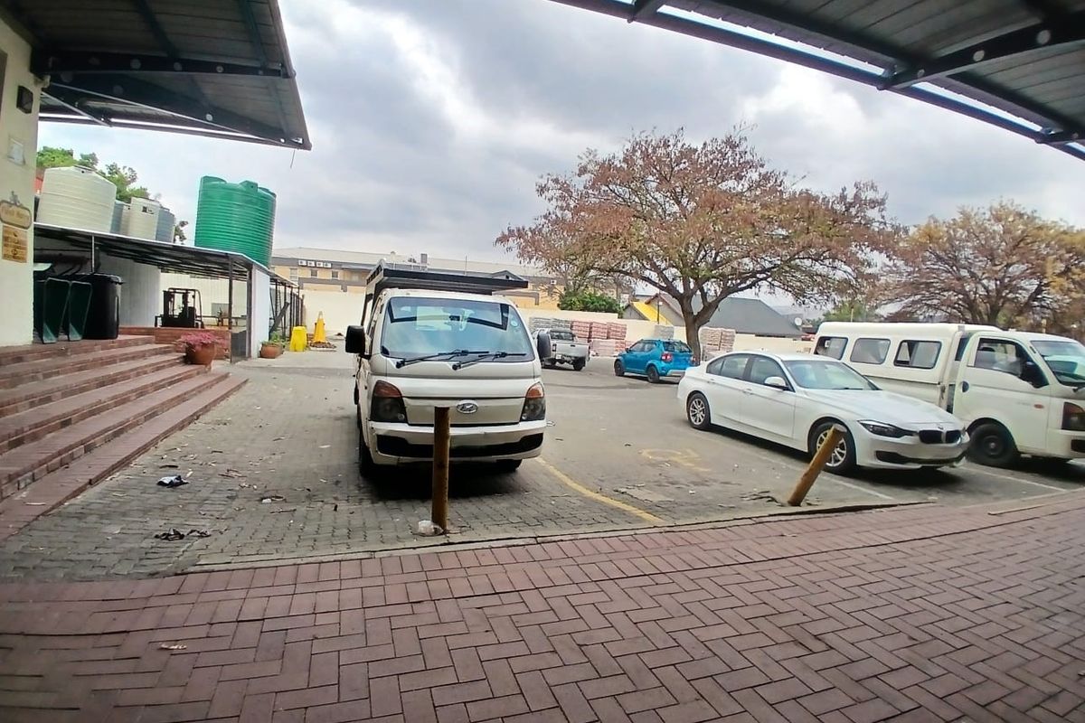 Exterior rear view of a retail property featuring a paved parking area, covered structure, and water storage tanks.