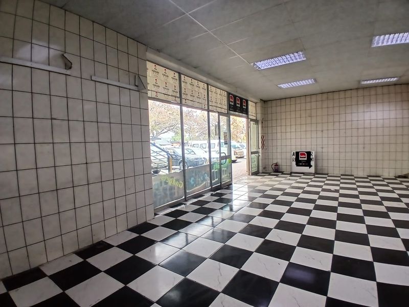 Empty retail space featuring a checkered tiled floor, tiled walls, and a large glass storefront providing natural light and street visibility.