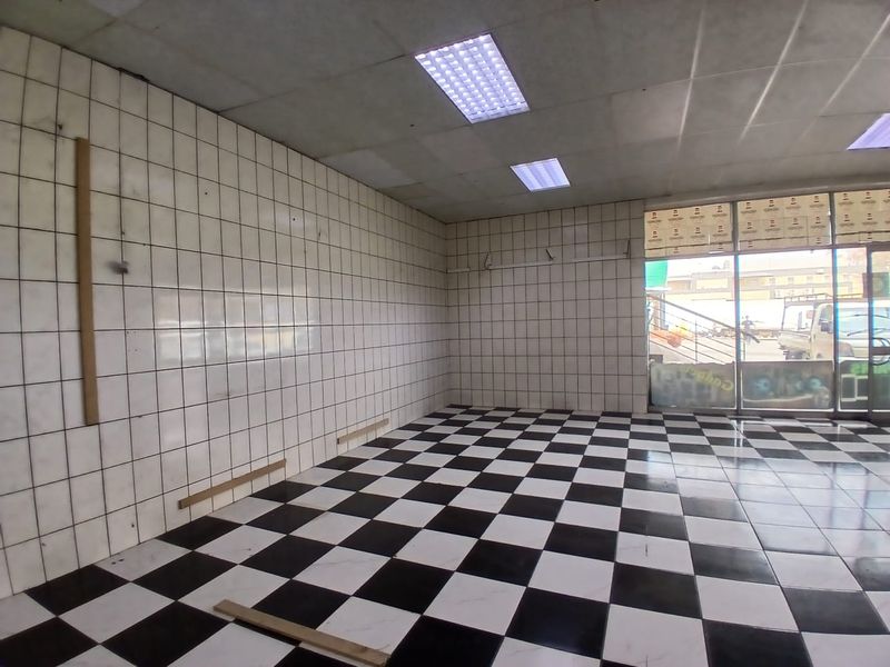 Empty retail space featuring checkered floor tiles, tiled walls, and large glass storefront windows, suitable for a variety of commercial business applications.