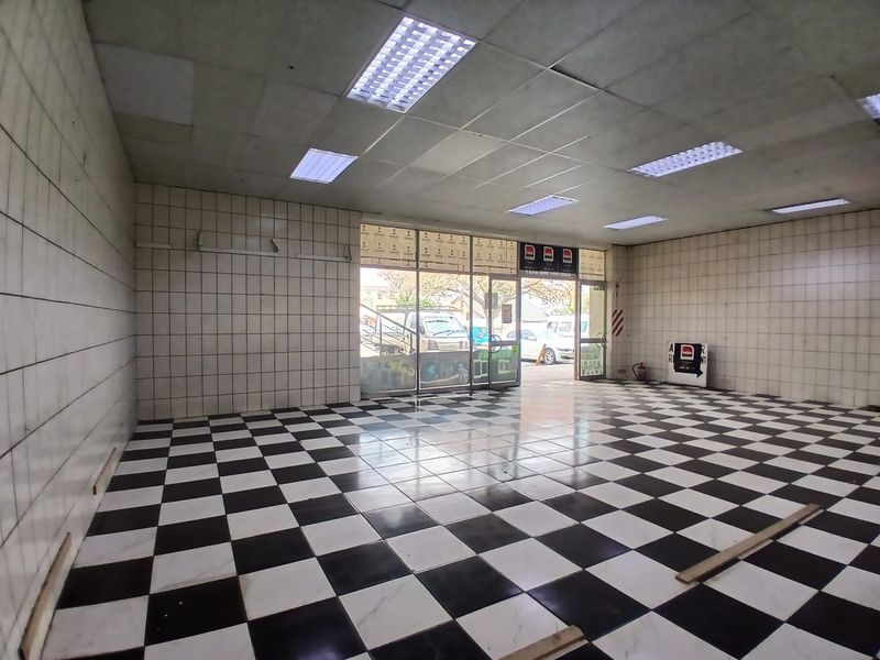 Empty retail space featuring checkered floor tiles, tiled walls, and a glass storefront entrance with recessed ceiling lighting.