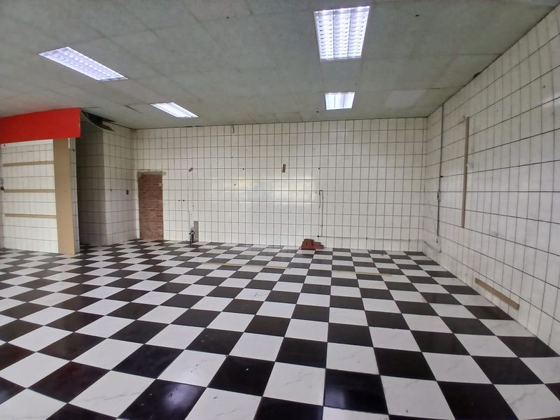 An empty, open-plan retail space featuring checkered floor tiles, tiled walls, and recessed fluorescent lighting, ready for renovation or custom fit-out.