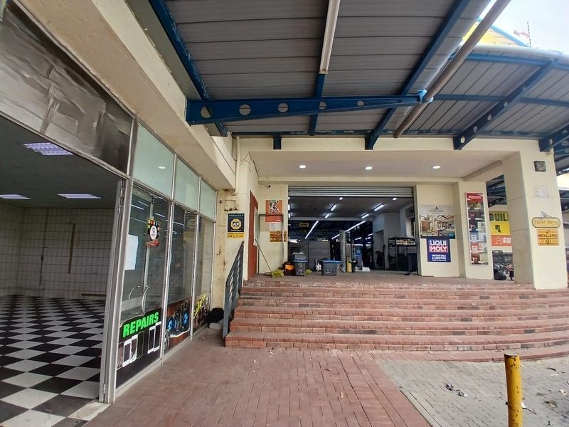 Front entrance of a retail unit featuring a covered walkway, brick stairs, and a glass storefront with security roller shutters.