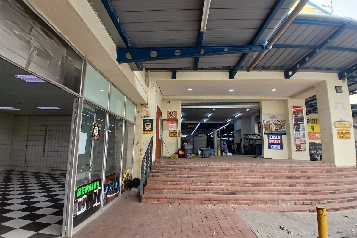 Front entrance of a retail unit featuring a covered walkway, brick stairs, and a glass storefront with security roller shutters.