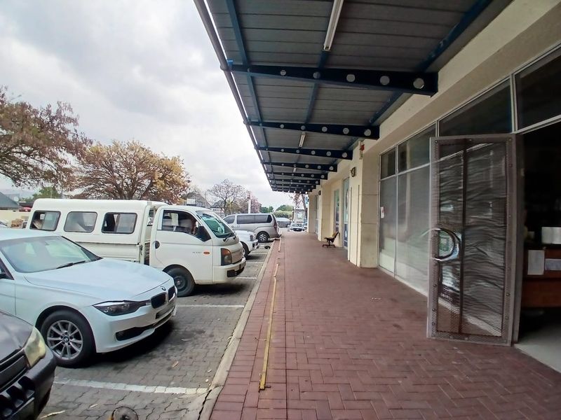 Exterior view of a retail storefront featuring a covered walkway, paved sidewalk, and large glass display windows with metal security access.