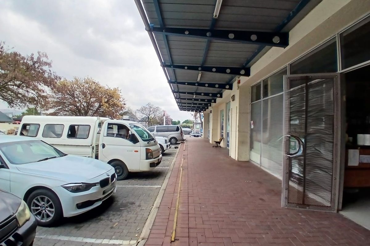 Exterior view of a retail storefront featuring a covered walkway, paved sidewalk, and large glass display windows with metal security access.
