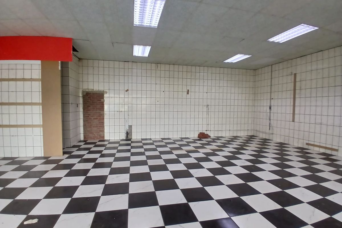 An empty retail space featuring a black and white checkered tiled floor, tiled walls, and recessed fluorescent lighting, requiring cosmetic refurbishment.