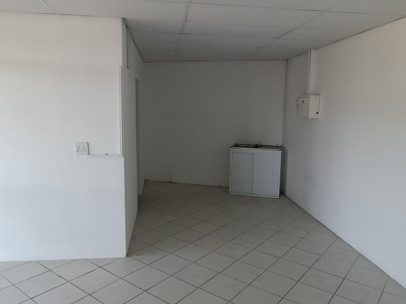 An empty utility space featuring tiled flooring, a drop ceiling, and a small kitchenette cabinet with a sink.