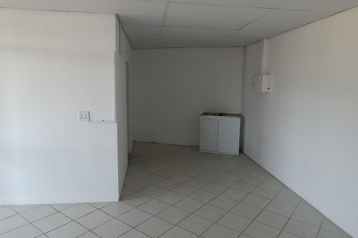 An empty utility space featuring tiled flooring, a drop ceiling, and a small kitchenette cabinet with a sink.