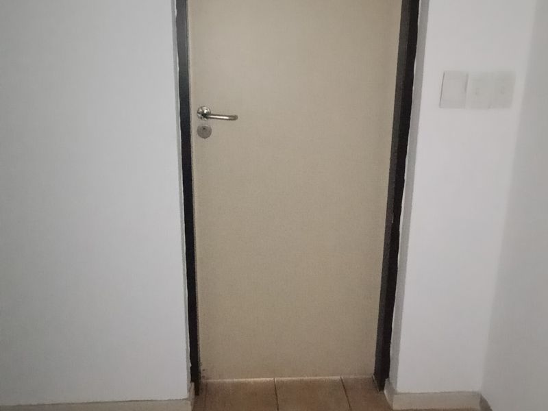 A simple office hallway featuring tiled flooring and an emergency exit sign above a standard interior door.