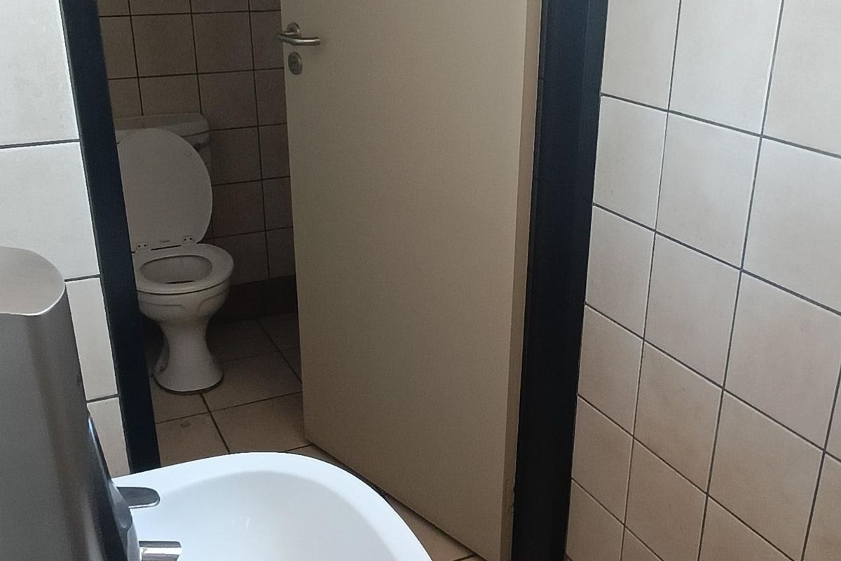A functional office bathroom featuring a wall-mounted basin, tiled walls and flooring, and a separate toilet cubicle.