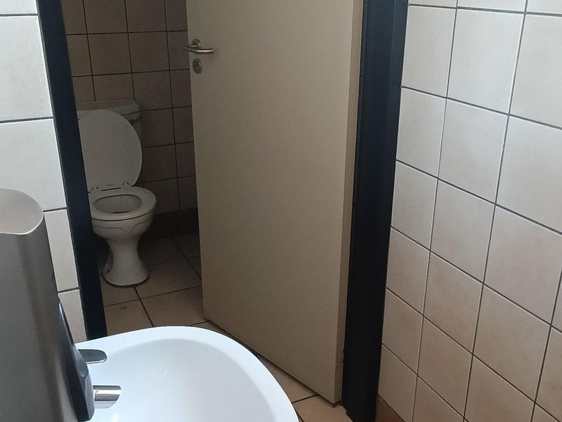 A functional office bathroom featuring a wall-mounted basin, tiled walls and flooring, and a separate toilet cubicle.