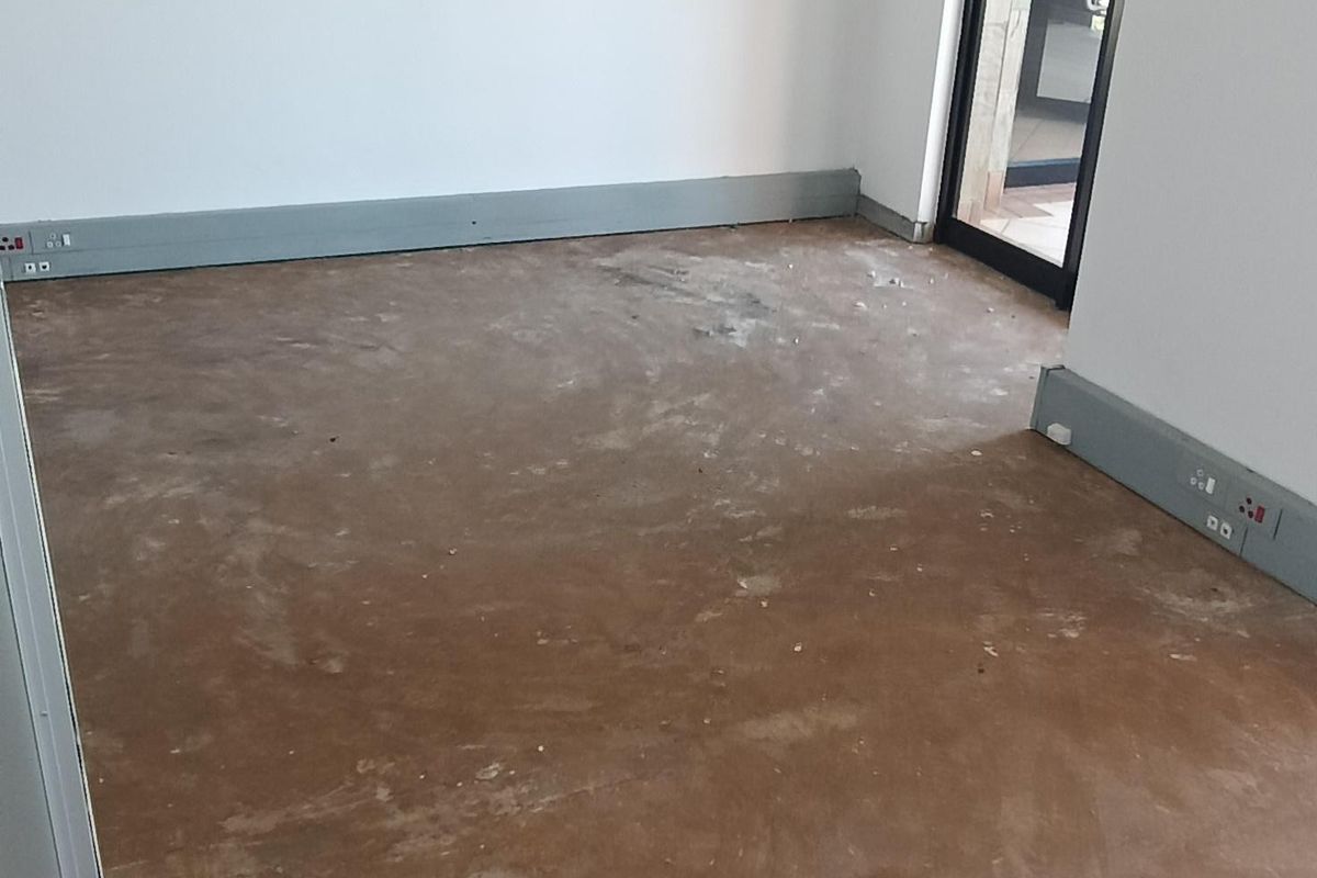 An empty office space featuring a suspended ceiling, recessed lighting, and perimeter trunking, currently awaiting final flooring installation.