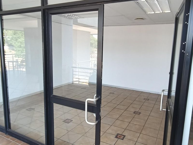 A vacant office space featuring aluminum-framed glass partitioning, tiled flooring, and a suspended ceiling with integrated lighting.