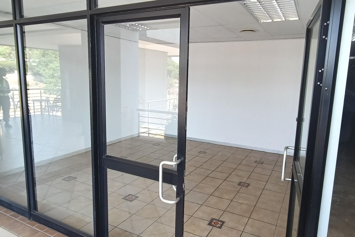 A vacant office space featuring aluminum-framed glass partitioning, tiled flooring, and a suspended ceiling with integrated lighting.