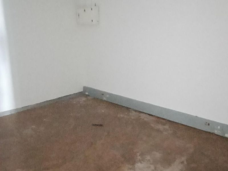 An empty office space featuring a suspended ceiling with recessed lighting and worn flooring, ready for refurbishment or fit-out.