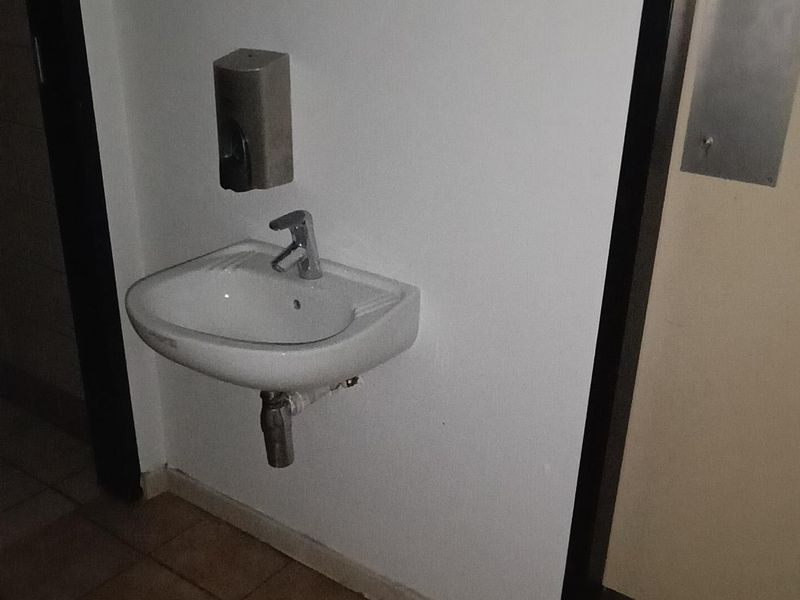 A functional office bathroom area featuring a wall-mounted basin, chrome faucet, and tiled flooring.