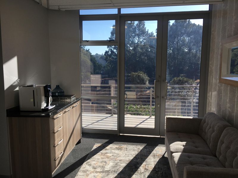 A bright office space featuring built-in cabinetry with a granite countertop and direct access to a private balcony with scenic views.