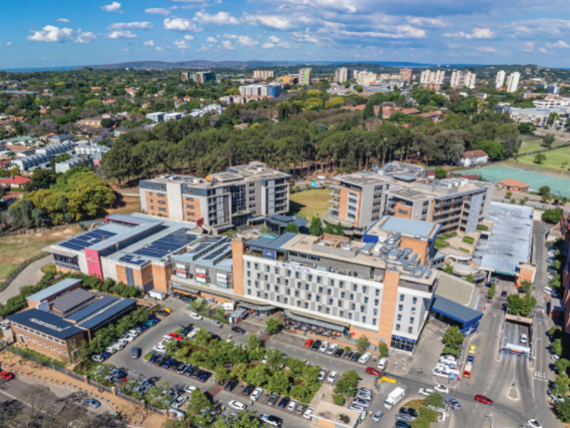 Aerial view of a large commercial office and retail complex featuring extensive parking facilities, solar panel installations, and proximity to a stadium.