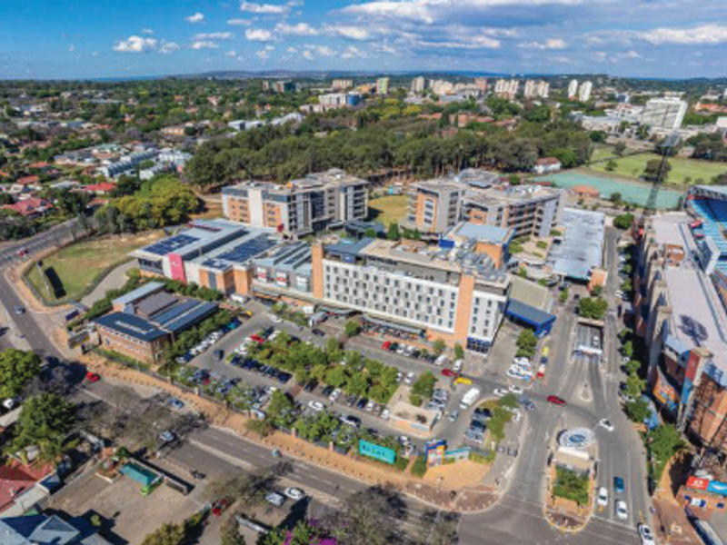 Aerial view of a large office complex featuring multiple buildings, extensive parking facilities, and solar panel installations in an urban setting.