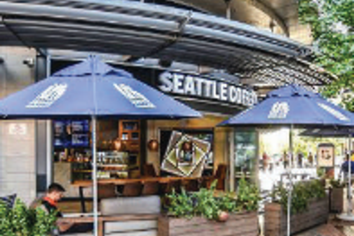 Outdoor seating area for a coffee shop featuring a curved concrete canopy, paved flooring, and integrated wooden planters.