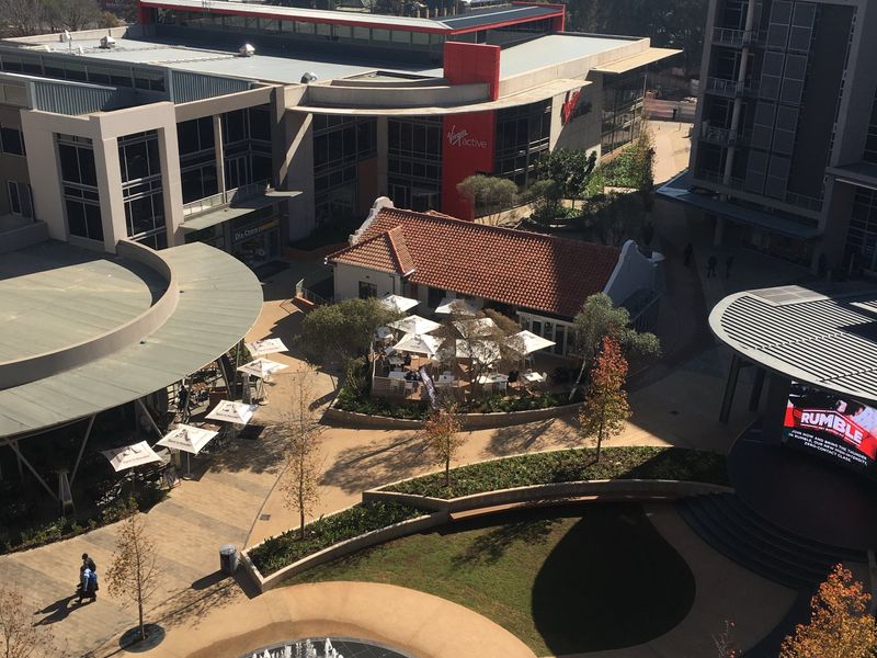 An aerial view of a modern commercial office and retail complex featuring landscaped courtyards, a central fountain, and outdoor dining areas.