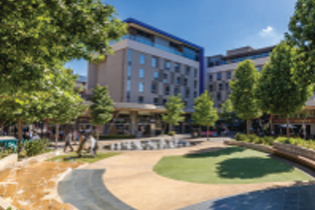 A well-maintained office complex courtyard featuring landscaped gardens, a central water feature, and paved walkways between multi-story commercial buildings.