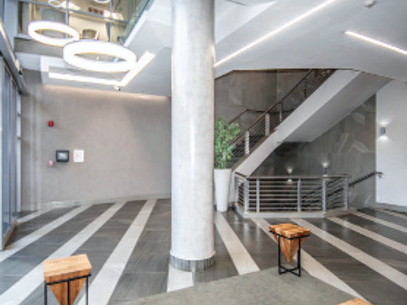Modern office building entrance lobby featuring a grand staircase, contemporary pendant lighting, and high-quality tiled flooring with a spacious open-plan layout.