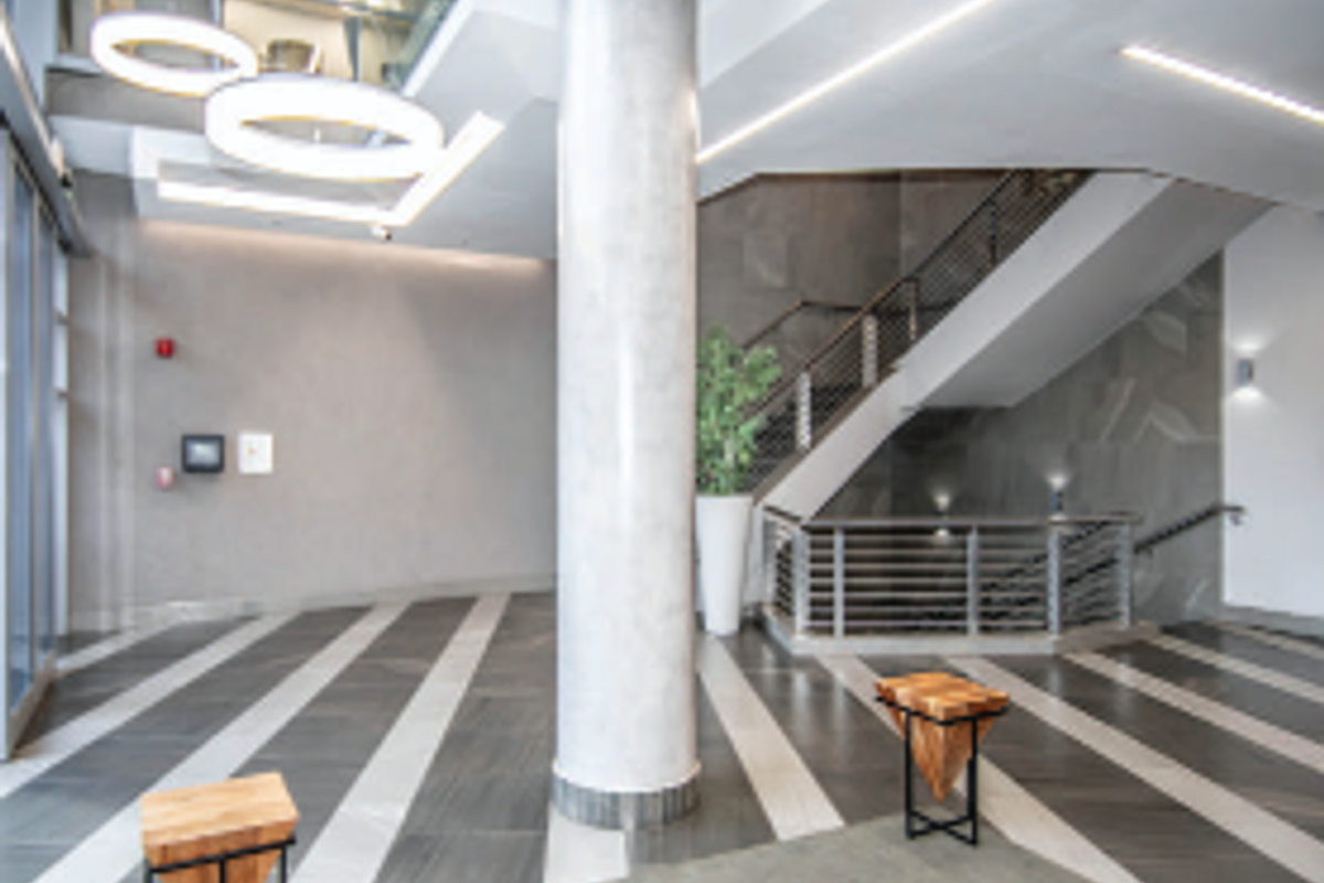 Modern office building entrance lobby featuring a grand staircase, contemporary pendant lighting, and high-quality tiled flooring with a spacious open-plan layout.