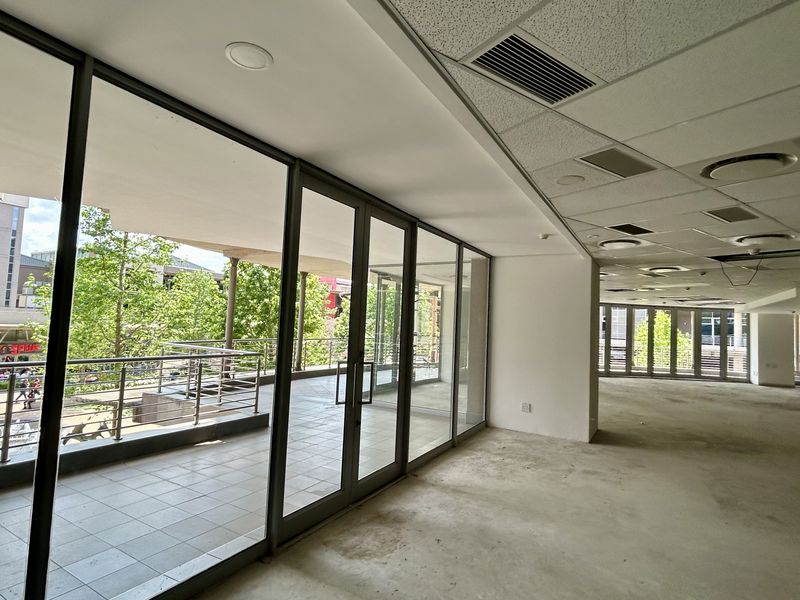 Spacious open-plan office area featuring a suspended ceiling, recessed lighting, and direct access to a private balcony through floor-to-ceiling glass doors.