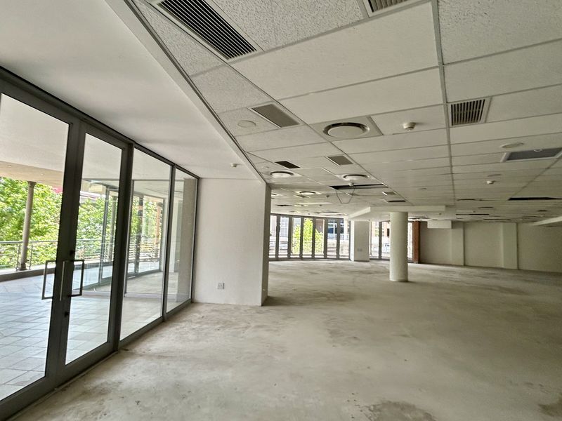 Spacious open-plan office area featuring floor-to-ceiling glass doors, suspended ceilings, and direct access to an outdoor balcony.