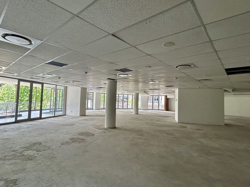 Spacious open-plan office area featuring a suspended ceiling, structural columns, and large sliding glass doors leading to an outdoor balcony.