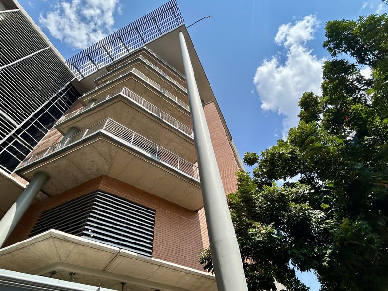 Low-angle view of a modern multi-story office building featuring brick cladding, concrete balconies, and architectural metal louvres.