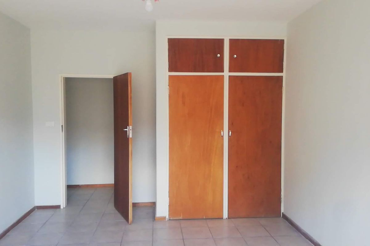 A bedroom featuring tiled flooring and built-in wooden cupboards with overhead storage compartments.