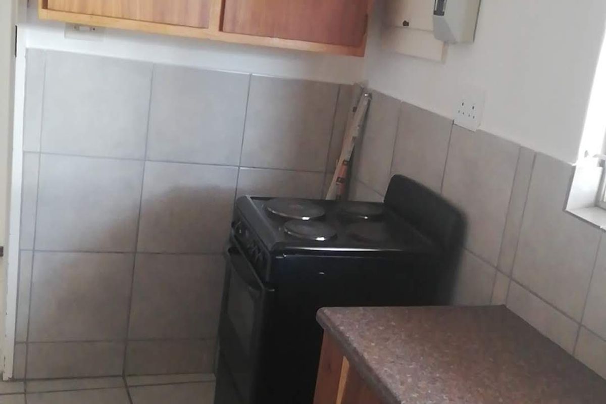 A compact kitchen featuring wooden cabinetry, tiled splashbacks, and a freestanding electric stove.