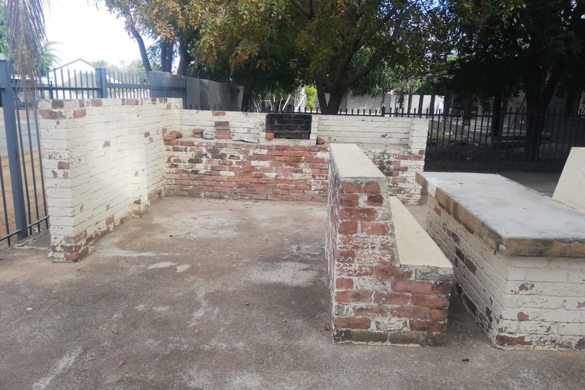 Outdoor entertainment area featuring a built-in brick braai and integrated concrete seating, set within a fenced garden space.