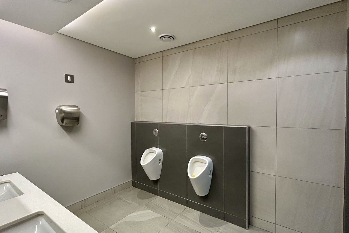 Modern office restroom featuring wall-mounted urinals, large-format wall tiling, recessed ceiling lighting, and a clean, minimalist aesthetic.