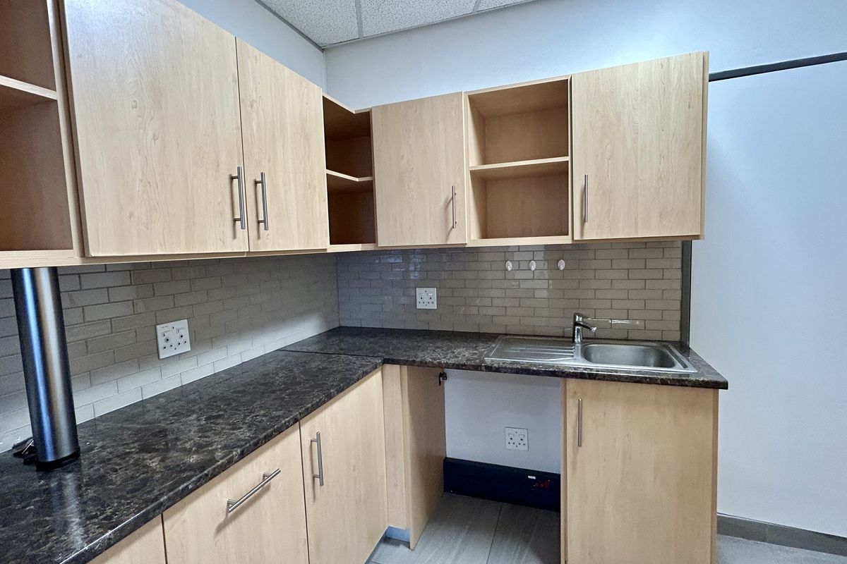 A clean, functional office kitchenette featuring light wood-finish cabinetry, dark laminate countertops, and a modern subway tile backsplash.