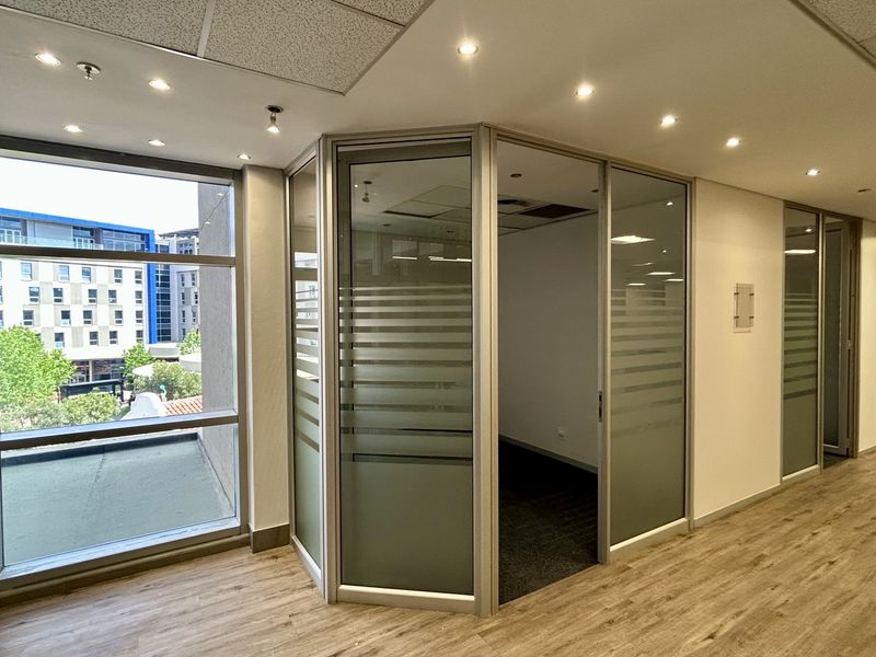 Modern office space featuring glass partitions, recessed lighting, and wood-look flooring, offering a bright and professional work environment.