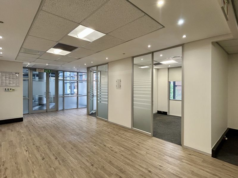 Modern open-plan office space featuring glass partitioned offices, suspended ceilings with recessed lighting, and a combination of laminate and carpet flooring.