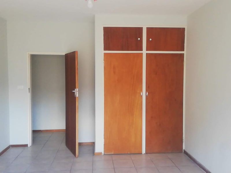 A bedroom featuring tiled flooring and built-in wooden cupboards with overhead storage compartments.