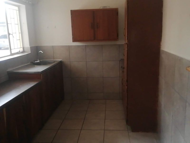 A functional kitchen featuring wooden cabinetry, tiled splashbacks, and a stainless steel sink, offering a dated aesthetic ready for modernization.
