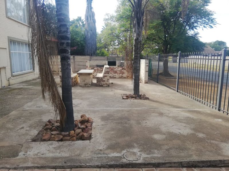 Outdoor patio area featuring a built-in brick braai and seating, set within a paved courtyard enclosed by metal fencing.