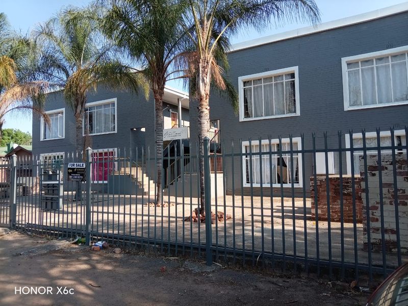 Exterior view of a two-story apartment building featuring dark grey painted brick facade, metal security fencing, and paved front courtyard area.