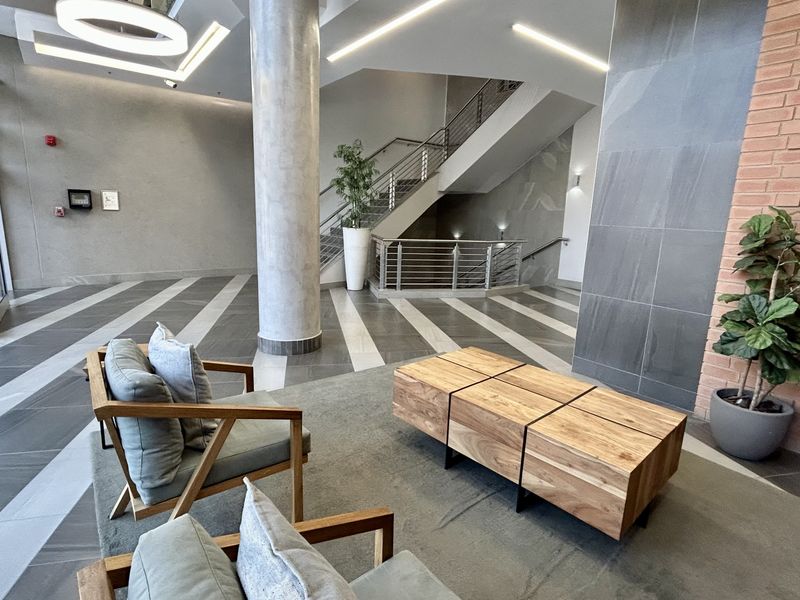 Modern office building lobby featuring a grand staircase, polished tiled flooring, exposed brick accents, and a prominent structural concrete column.