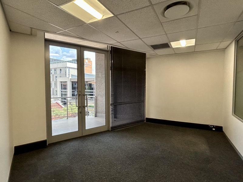 A vacant office space featuring a suspended ceiling, recessed lighting, carpeted flooring, and a glass door leading to a private balcony.