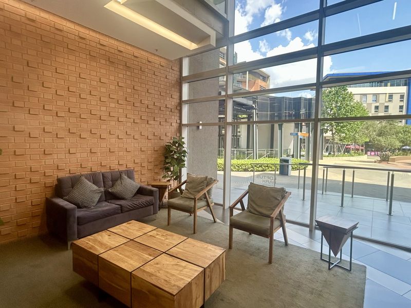 Modern office reception area featuring a striking exposed brick wall, floor-to-ceiling glass windows, and high-quality tiled flooring with ample natural light.